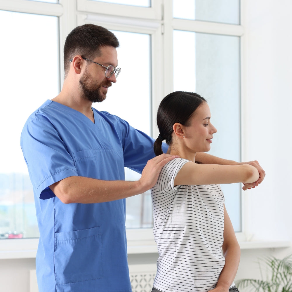 Physiotherapeut hilft einer Frau bei einer Schulterübung. Er führt ihren Arm, während sie die Bewegung aktiv mitmacht.