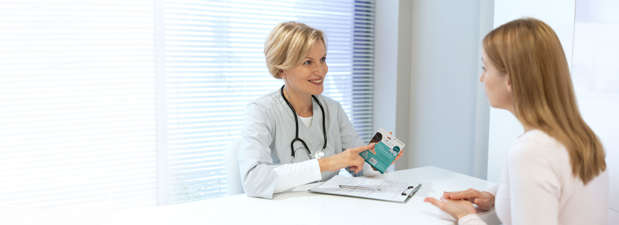 Ärztin im Gespräch mit einer Patientin in einer hellen Praxis. Sie hält eine Produktverpackung der TJ-Motion in der Hand und erklärt etwas dazu, während die Patientin zuhört.