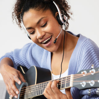 Eine Junge Frau trägt ein Headset, spielt Gitarre und singt.