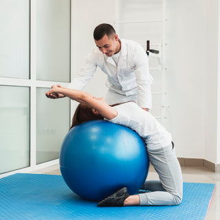 Therapeut unterstützt eine Frau bei einer Dehnübung auf einem großen blauen Gymnastikball. Die Frau lehnt sich rückwärts über den Ball und streckt die Arme aus, während der Therapeut sie stabilisiert.