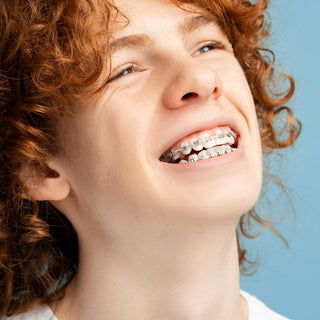 Ein Junge mit roten Locken und Zahnspange grinst mit geöffnetem Mund.